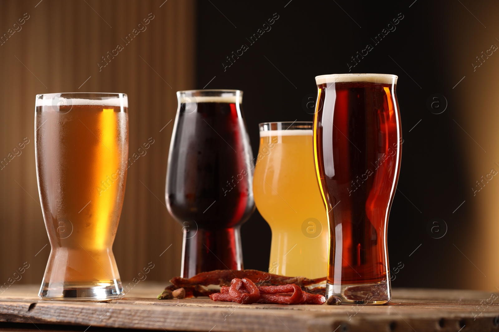 Photo of Glasses with different types of beer and snacks on wooden table against color background