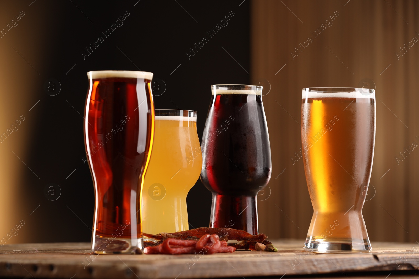 Photo of Glasses with different types of beer and snacks on wooden table against color background