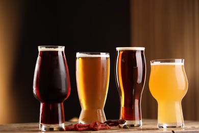 Photo of Glasses with different types of beer and snacks on wooden table against color background