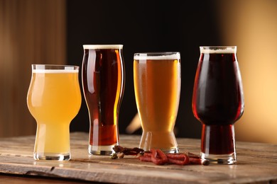 Photo of Glasses with different types of beer and snacks on wooden table against color background