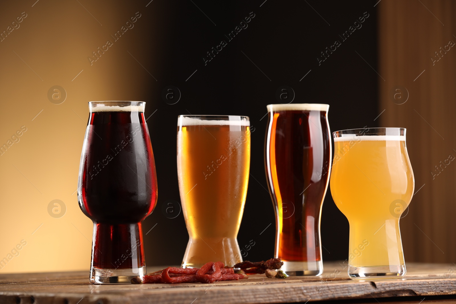 Photo of Glasses with different types of beer and snacks on wooden table against color background