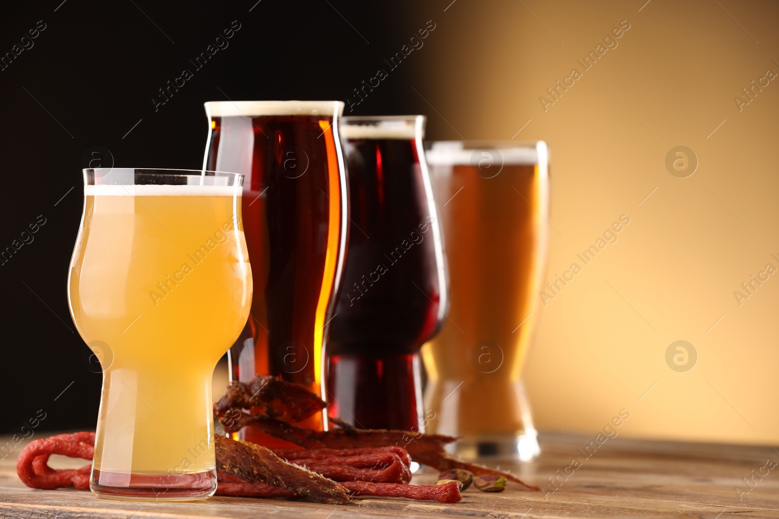 Photo of Glasses with different types of beer and snacks on wooden table against color background, closeup