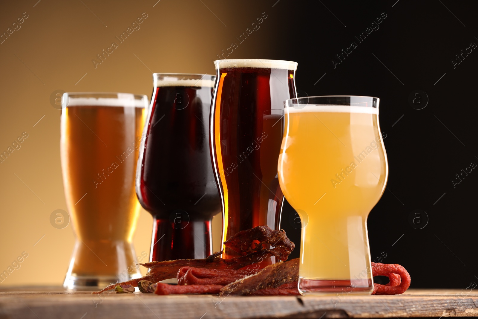 Photo of Glasses with different types of beer and snacks on wooden table against color background, closeup