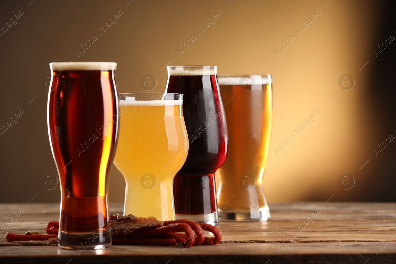 Photo of Glasses with different types of beer and snacks on wooden table against color background