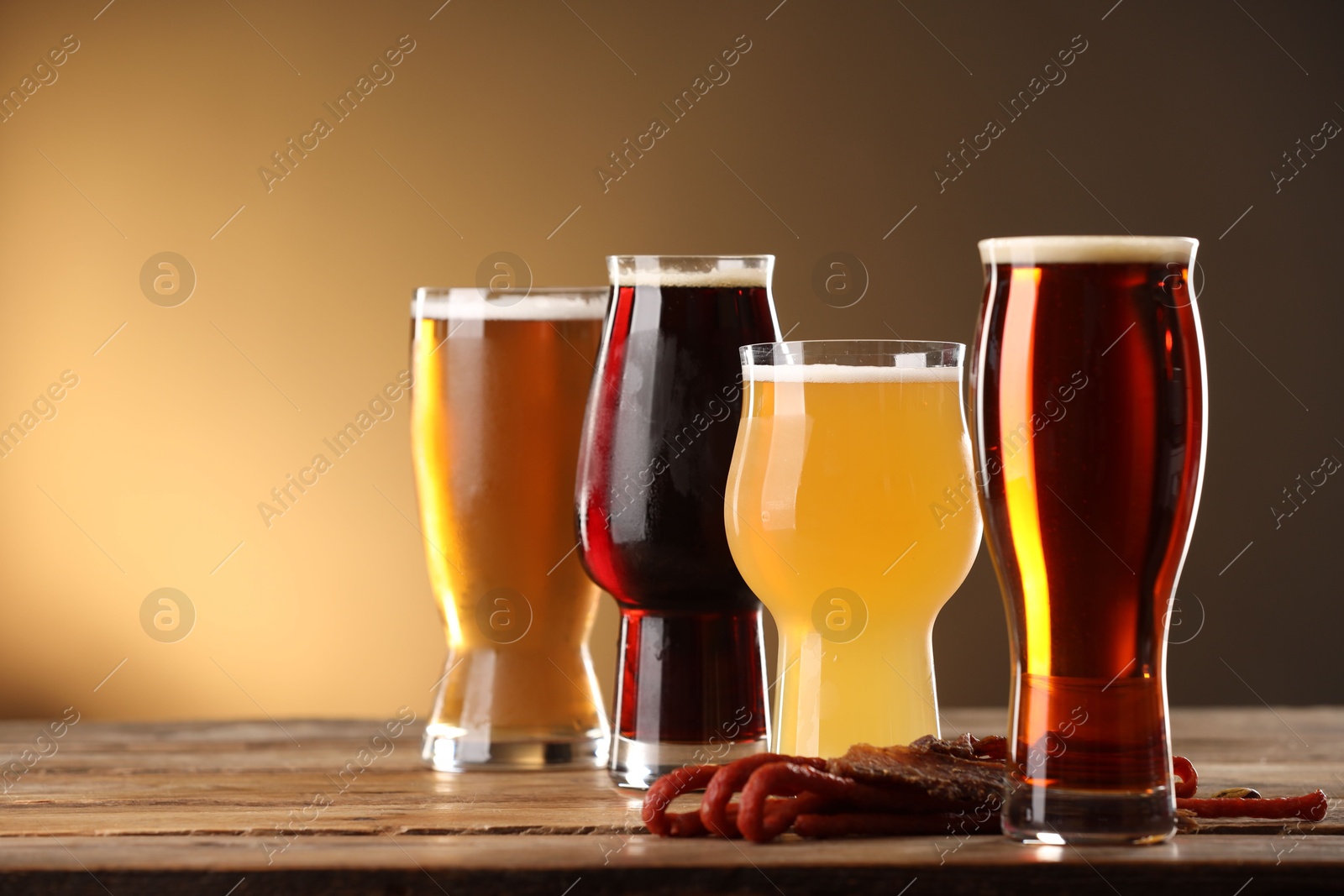 Photo of Glasses with different types of beer and snacks on wooden table against color background