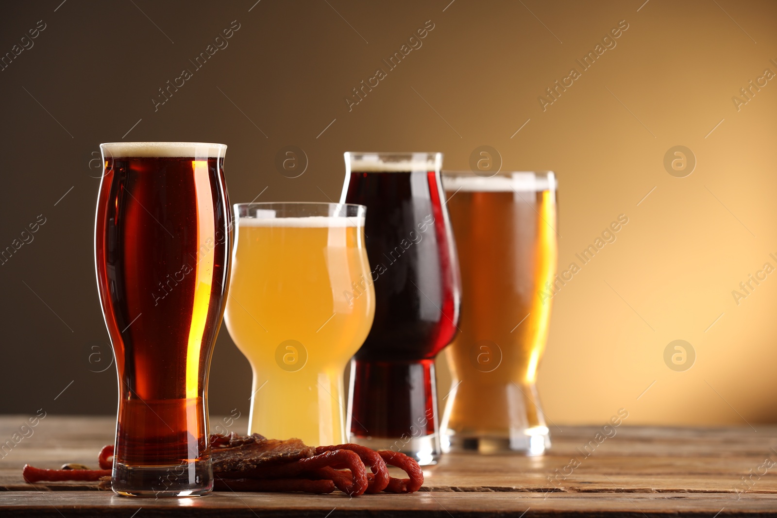 Photo of Glasses with different types of beer and snacks on wooden table against color background