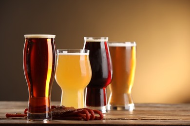 Photo of Glasses with different types of beer and snacks on wooden table against color background