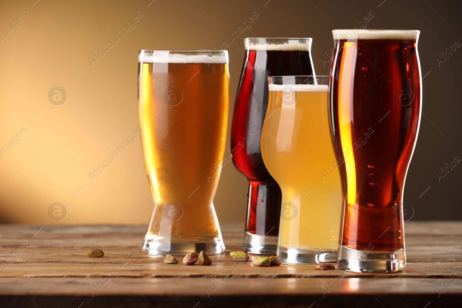 Photo of Glasses with different types of beer and pistachio nuts on wooden table against color background, closeup