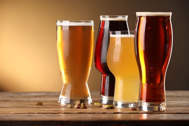 Photo of Glasses with different types of beer and pistachio nuts on wooden table against color background, closeup