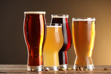 Photo of Glasses with different types of beer and pistachio nuts on wooden table against color background, closeup