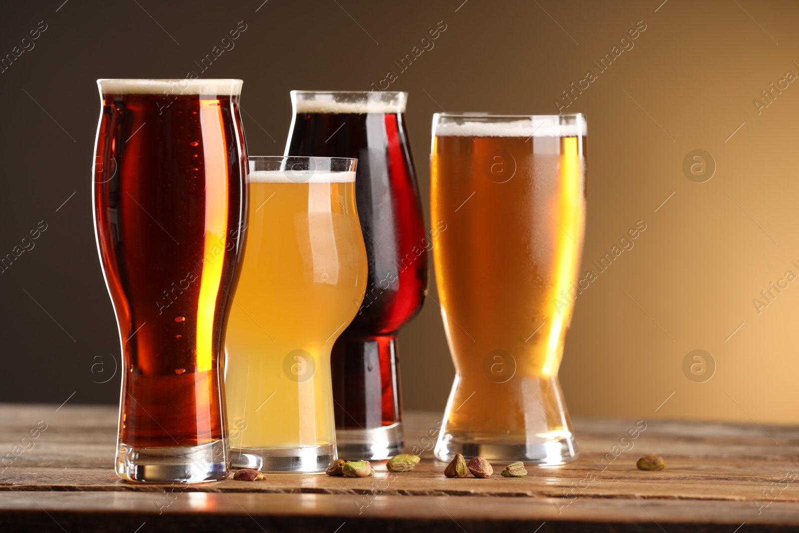 Photo of Glasses with different types of beer and pistachio nuts on wooden table against color background, closeup