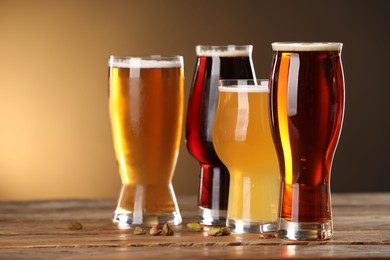 Photo of Glasses with different types of beer and pistachio nuts on wooden table against color background, closeup