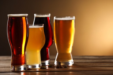 Photo of Glasses with different types of beer and pistachio nuts on wooden table against color background, closeup. Space for text