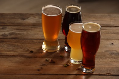 Photo of Glasses with different types of beer and pistachio nuts on wooden table