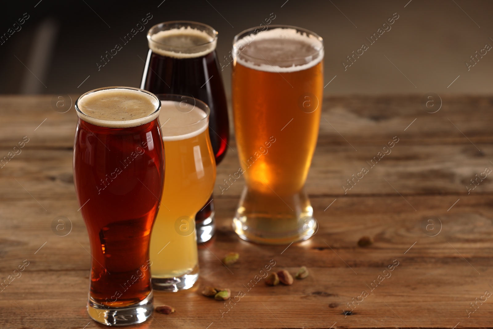 Photo of Glasses with different types of beer and pistachio nuts on wooden table