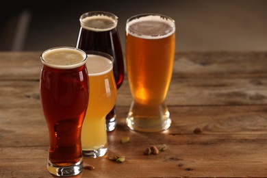 Photo of Glasses with different types of beer and pistachio nuts on wooden table