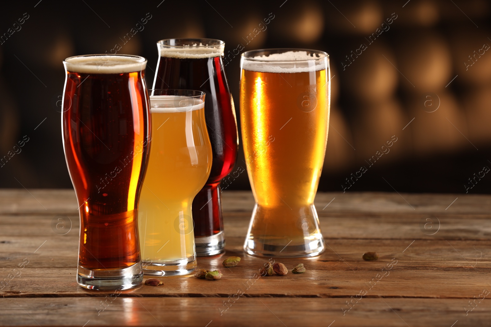 Photo of Glasses with different types of beer and pistachio nuts on wooden table indoors