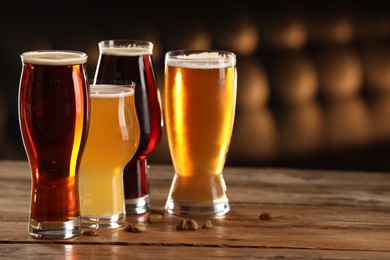 Photo of Glasses with different types of beer and pistachio nuts on wooden table indoors, space for text