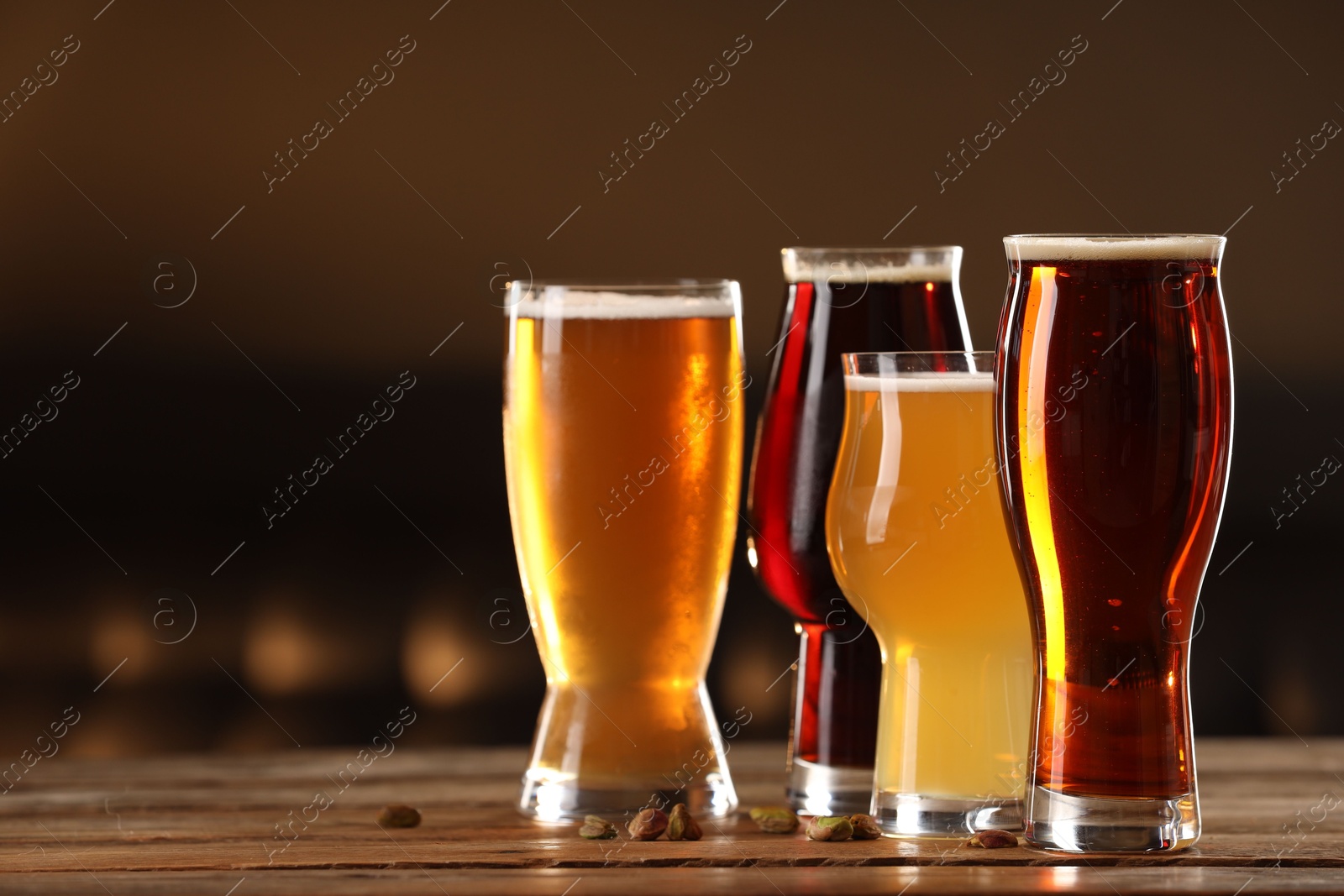 Photo of Glasses with different types of beer and pistachio nuts on wooden table indoors, space for text