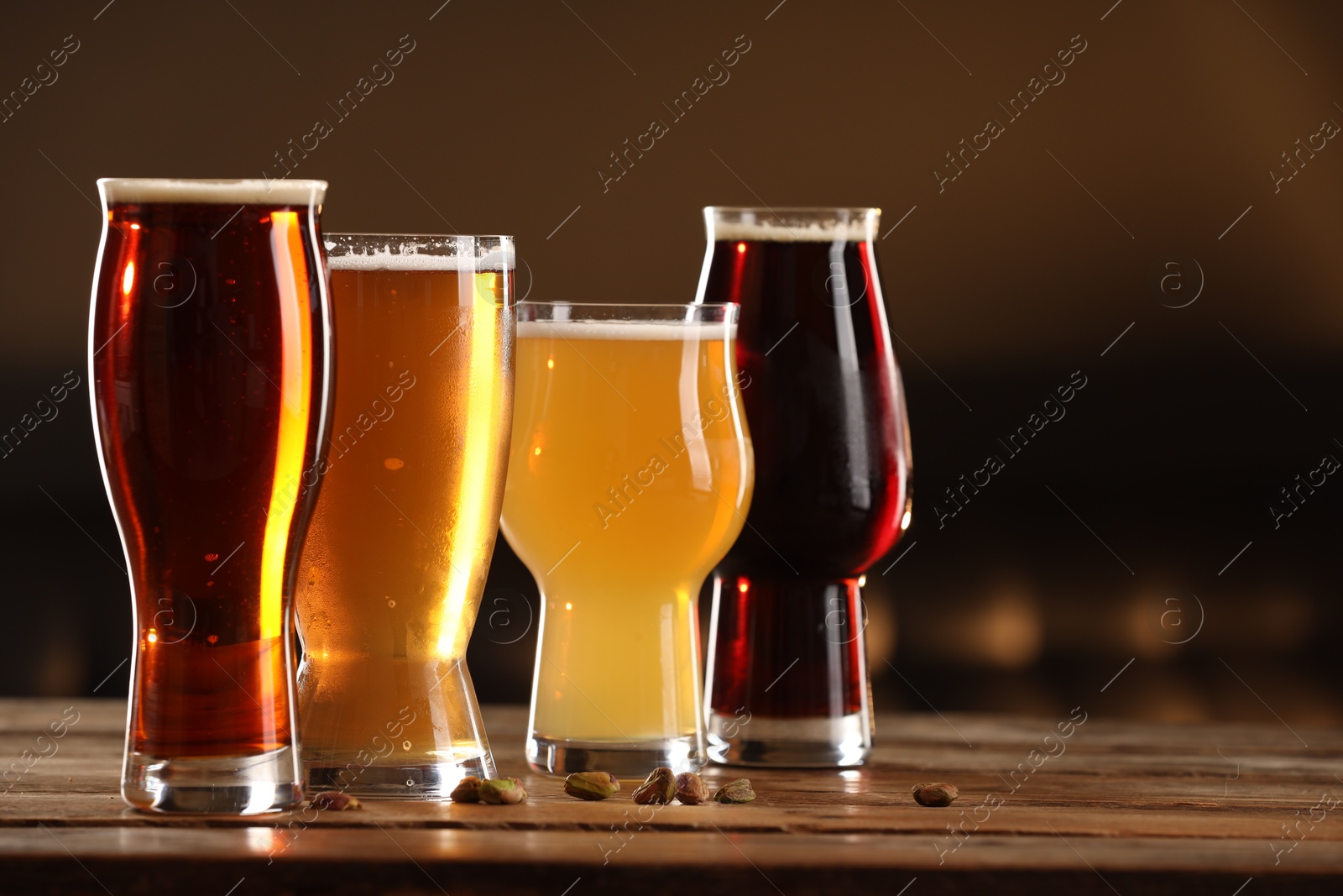 Photo of Glasses with different types of beer and pistachio nuts on wooden table indoors