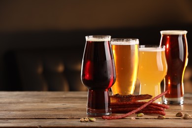 Photo of Glasses with different types of beer and snacks on wooden table indoors, space for text