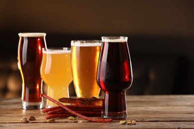 Photo of Glasses with different types of beer and snacks on wooden table indoors