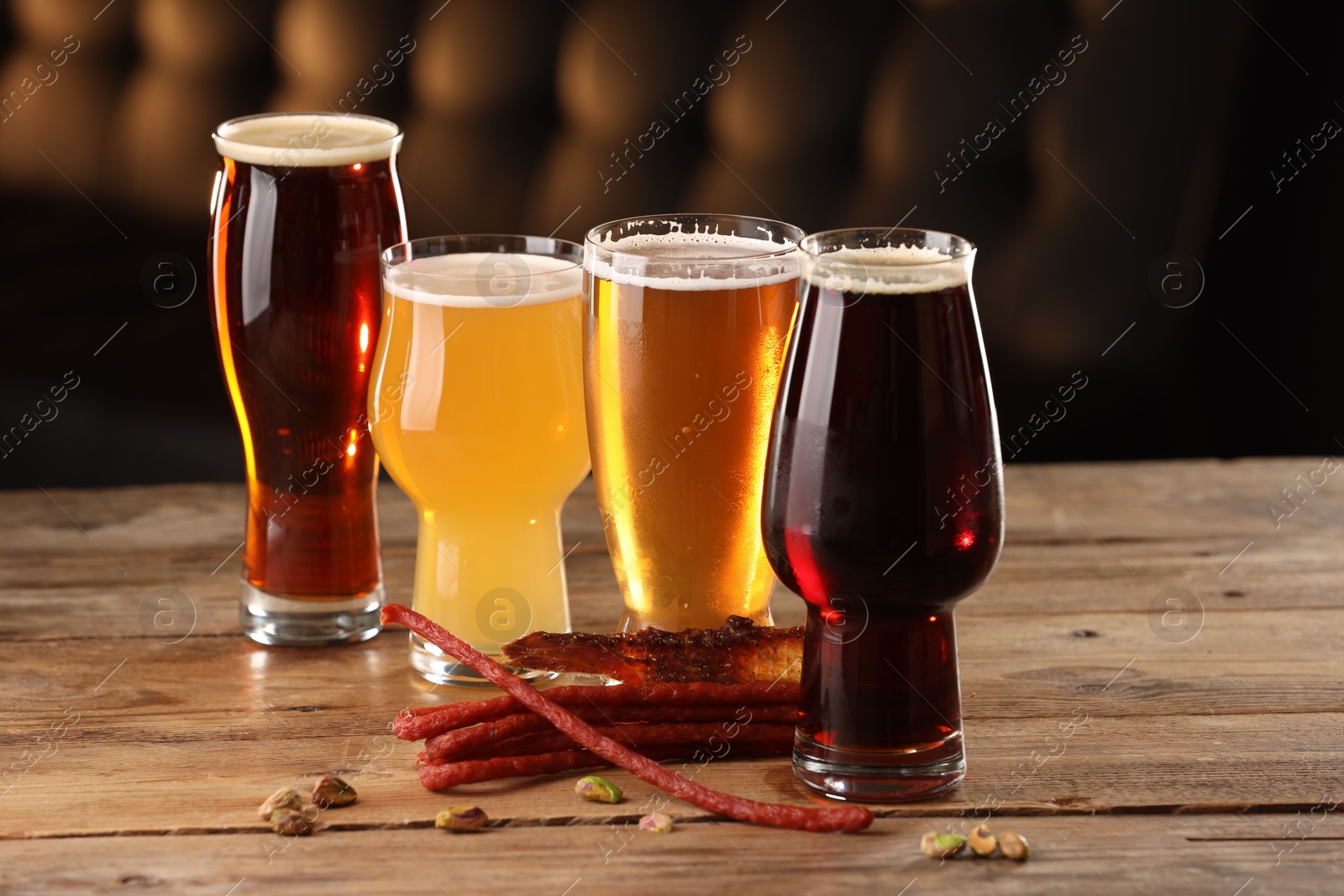 Photo of Glasses with different types of beer and snacks on wooden table indoors