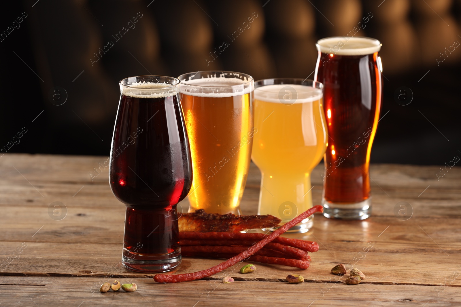 Photo of Glasses with different types of beer and snacks on wooden table indoors