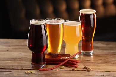 Photo of Glasses with different types of beer and snacks on wooden table indoors