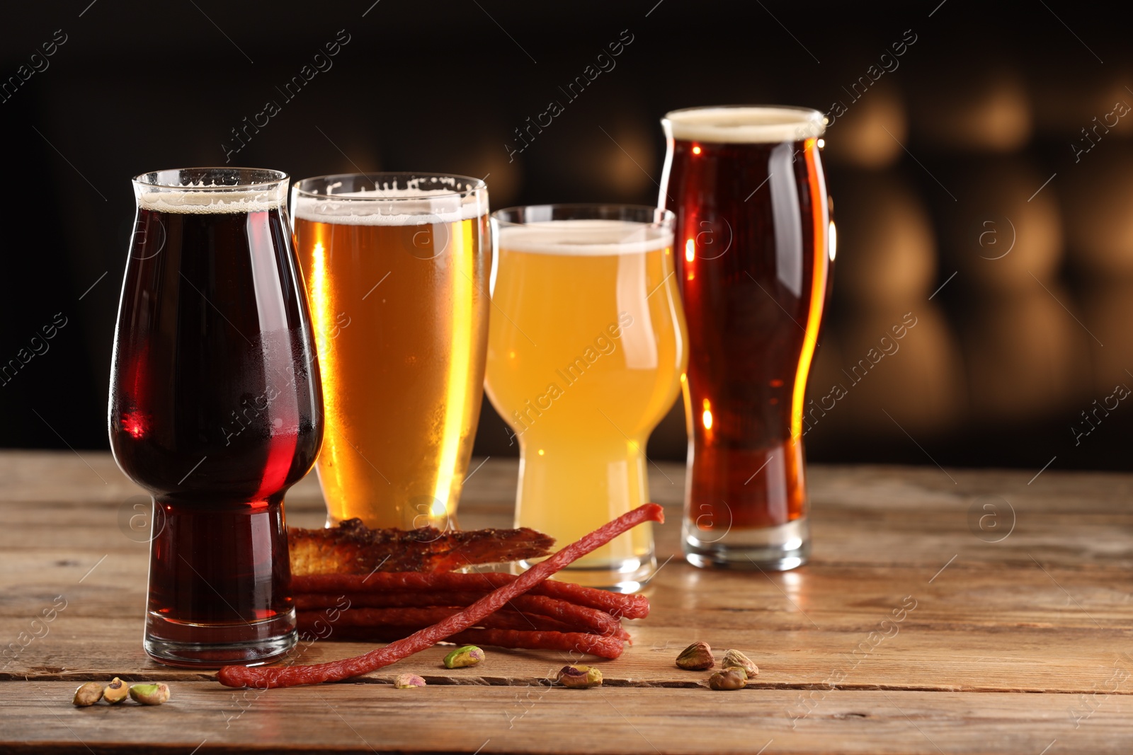 Photo of Glasses with different types of beer and snacks on wooden table indoors