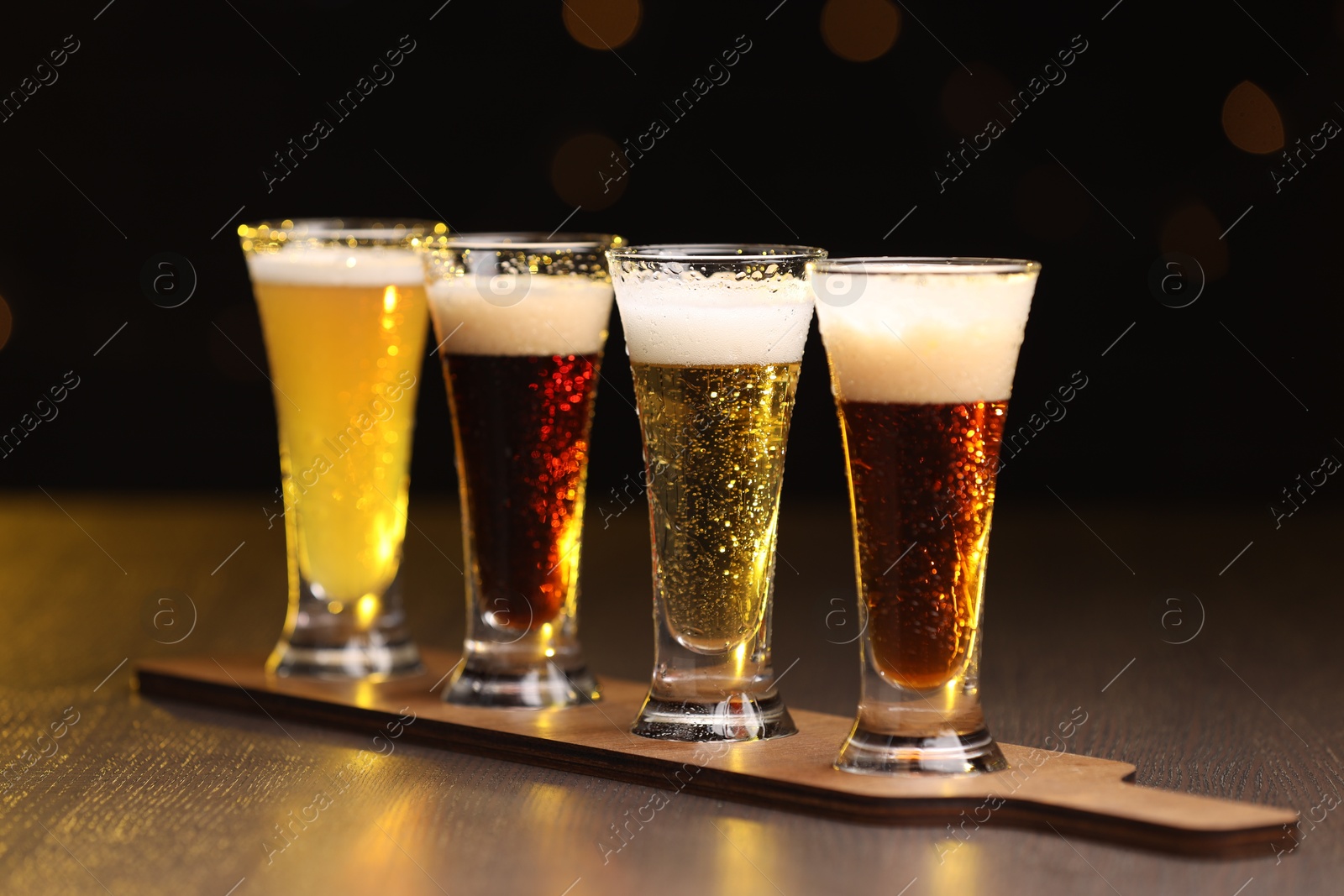 Photo of Glasses with different types of beer on wooden table against black background, closeup