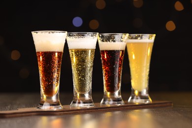 Photo of Glasses with different types of beer on wooden table against blurred lights, closeup