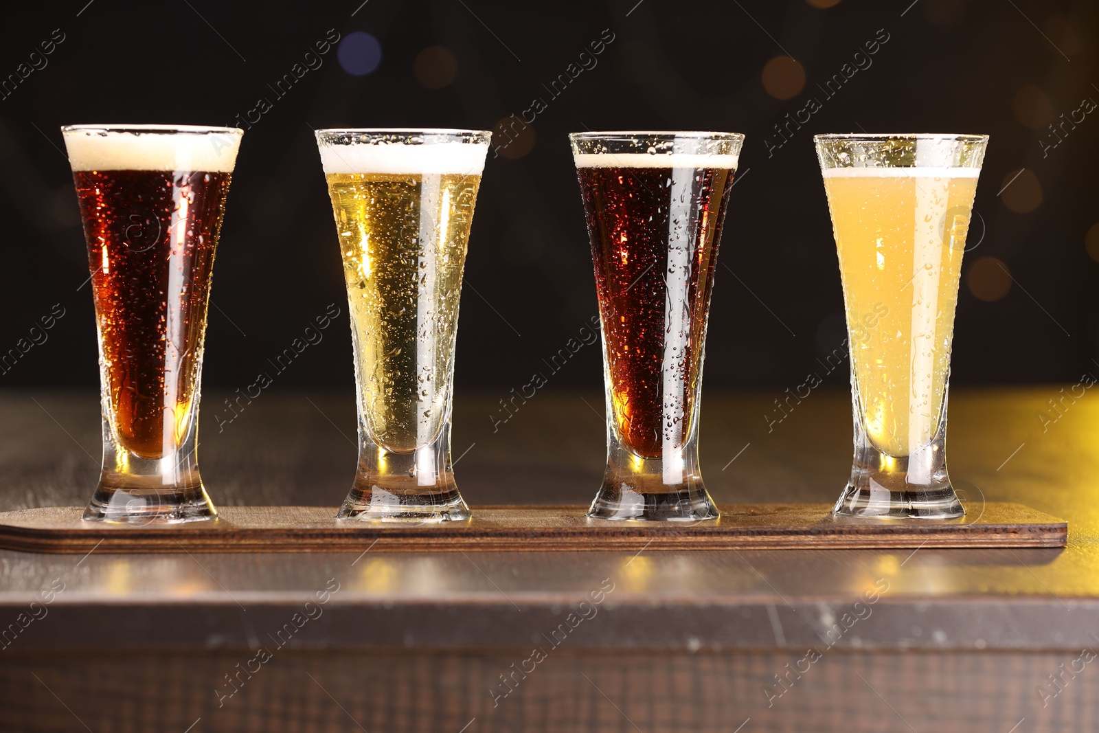 Photo of Glasses with different types of beer on wooden table against blurred lights, closeup