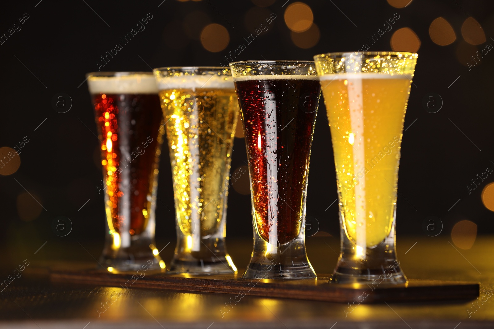 Photo of Glasses with different types of beer on wooden table against blurred lights, closeup