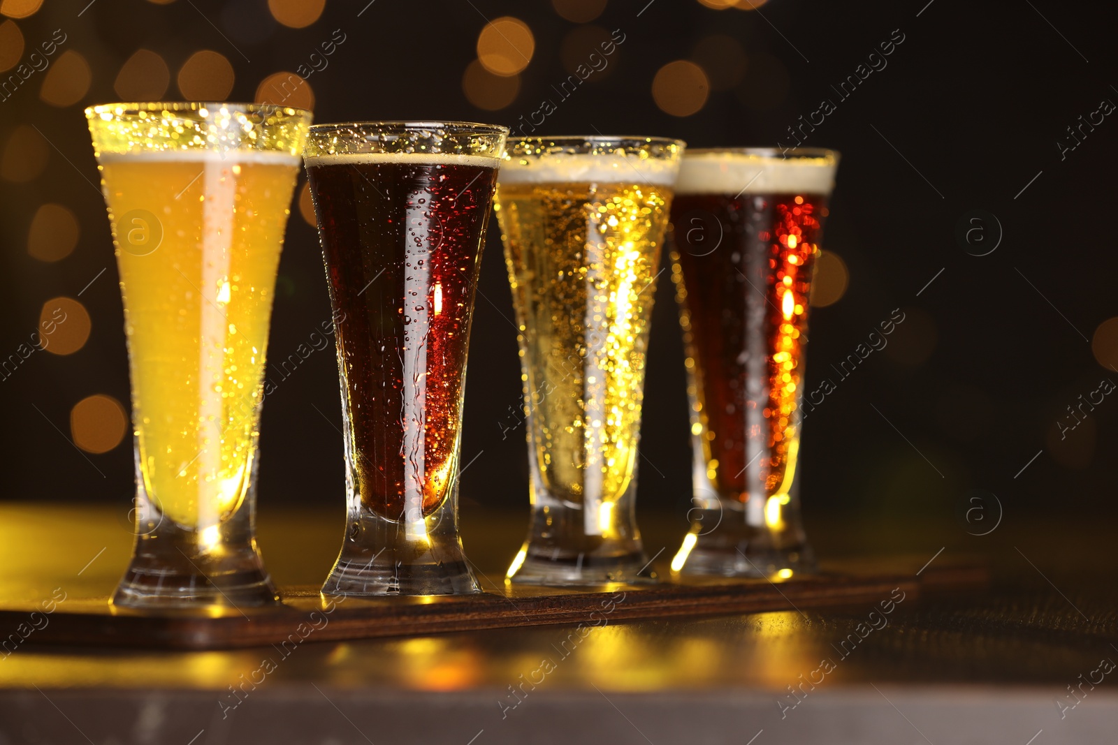 Photo of Glasses with different types of beer on wooden table against blurred lights, closeup