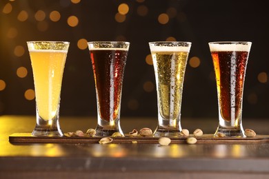 Photo of Glasses with different types of beer and pistachios on wooden table against blurred lights, closeup