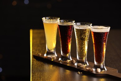 Photo of Glasses with different types of beer and pistachios on wooden table against black background, closeup. Space for text