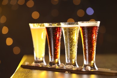 Photo of Glasses with different types of beer and pistachios on wooden table against blurred lights, closeup