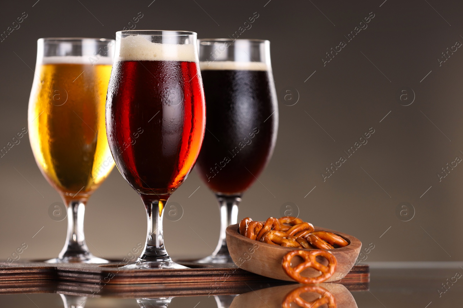 Photo of Glasses with different types of beer and snacks on mirror surface, closeup. Space for text