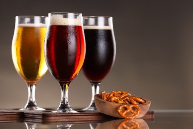 Photo of Glasses with different types of beer and snacks on mirror surface, closeup. Space for text