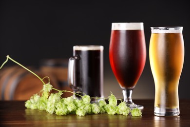 Photo of Glasses with different types of beer and fresh hops on wooden table in bar