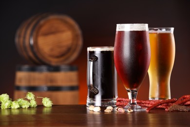 Photo of Glasses with different types of beer, snacks and fresh hops on wooden table in bar. Space for text