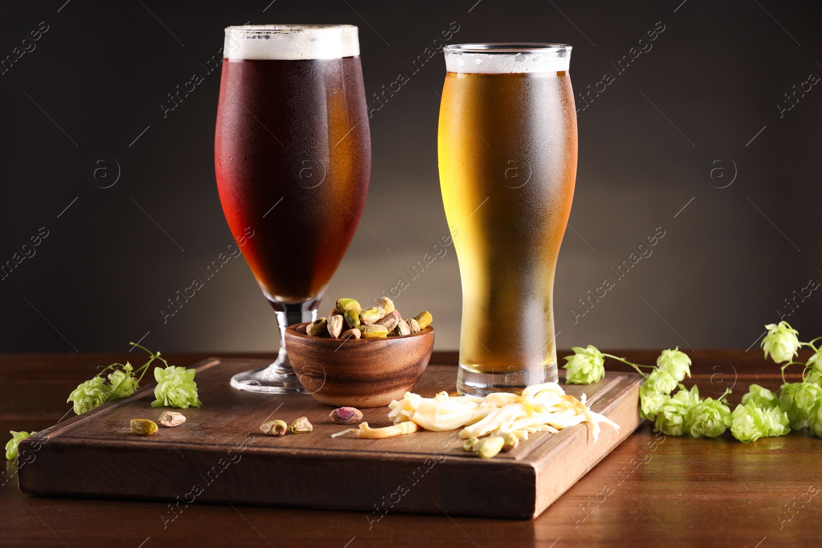 Photo of Glasses with different types of beer, snacks and fresh hops on wooden table