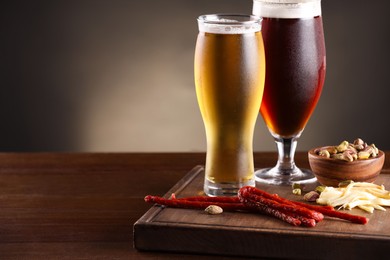 Photo of Glasses with different types of beer and snacks on wooden table, closeup. Space for text