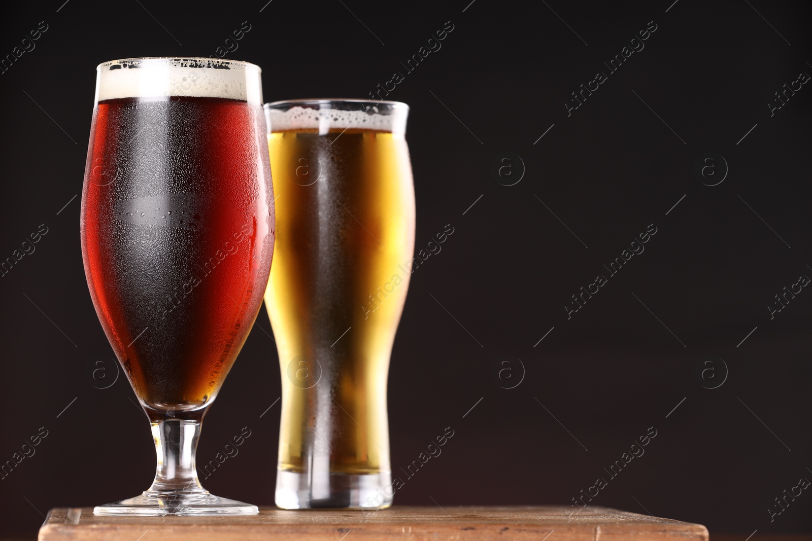 Photo of Glasses with different types of beer on board against black background, closeup. Space for text