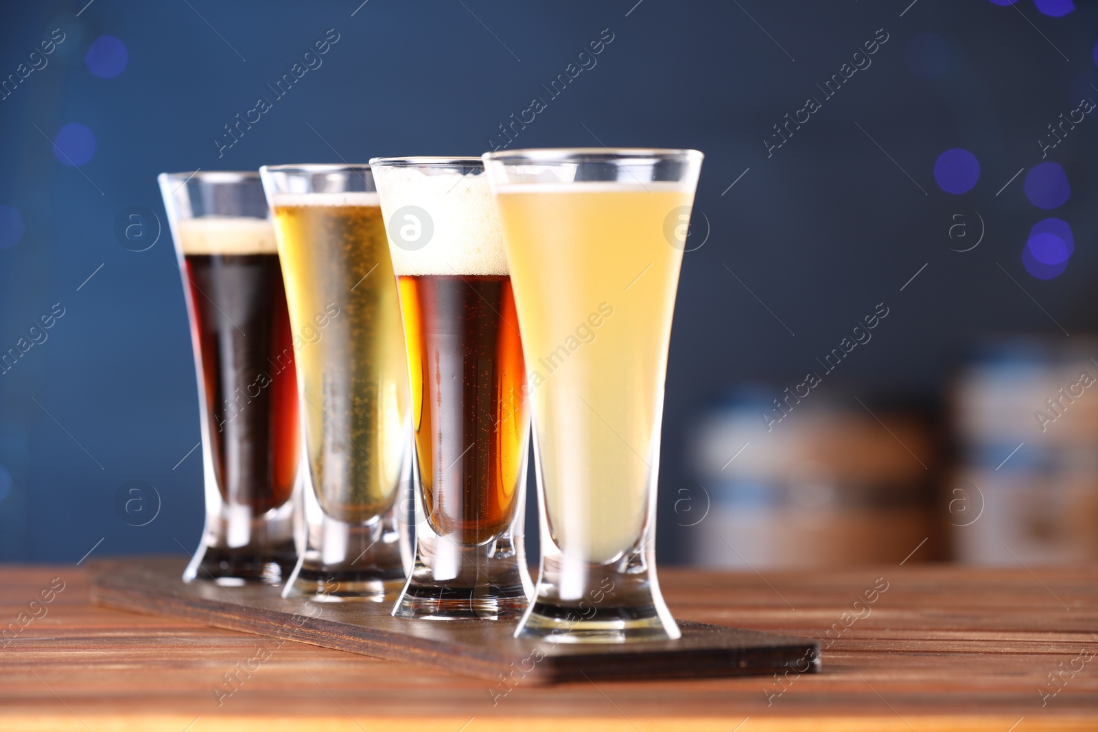 Photo of Glasses with different types of beer on wooden table against blue background, closeup