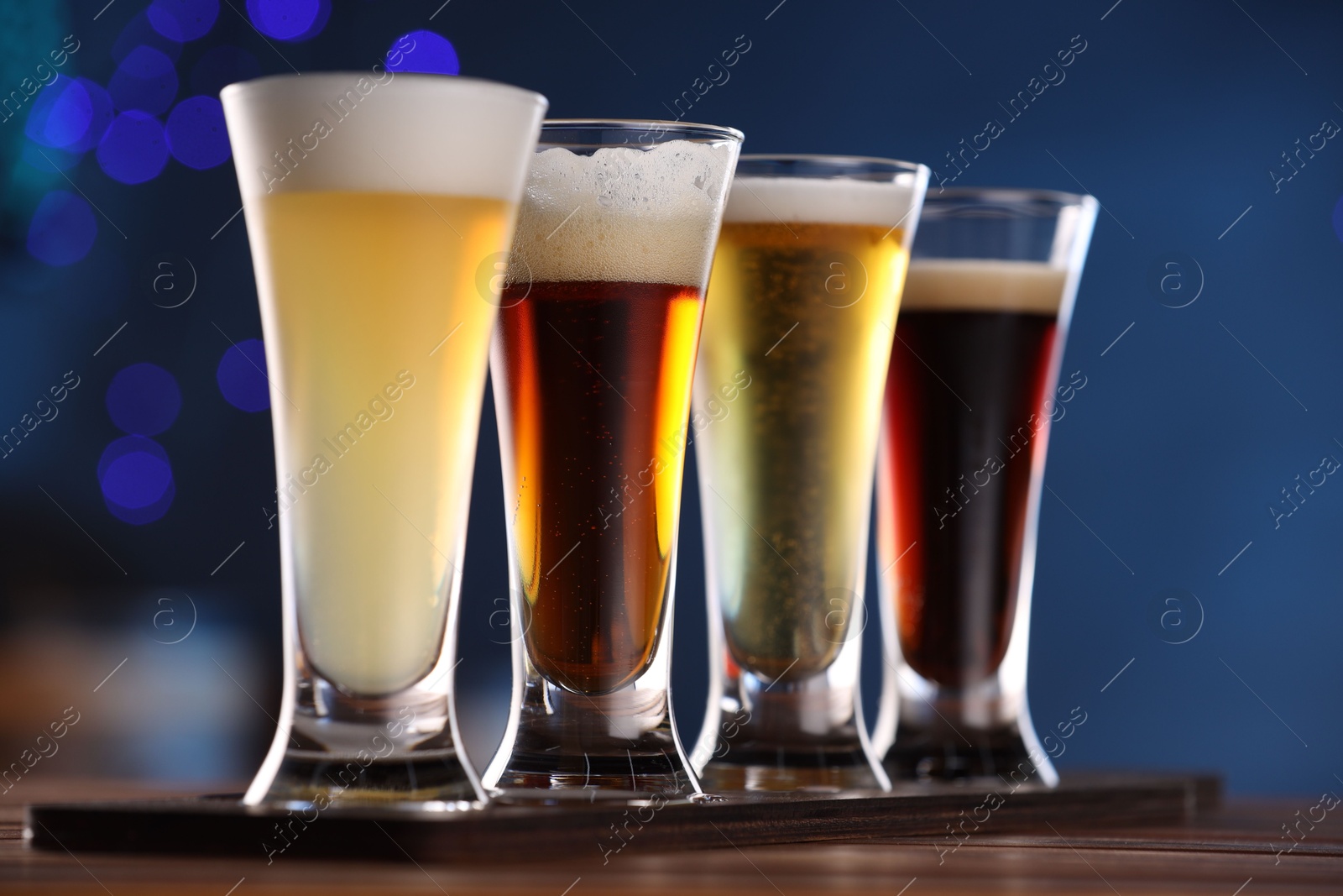 Photo of Glasses with different types of beer on wooden table against blue background, closeup