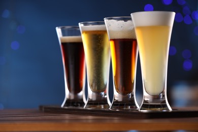 Photo of Glasses with different types of beer on wooden table against blue background, closeup. Space for text