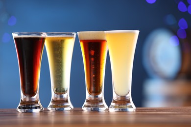 Photo of Glasses with different types of beer on wooden table against blue background, closeup