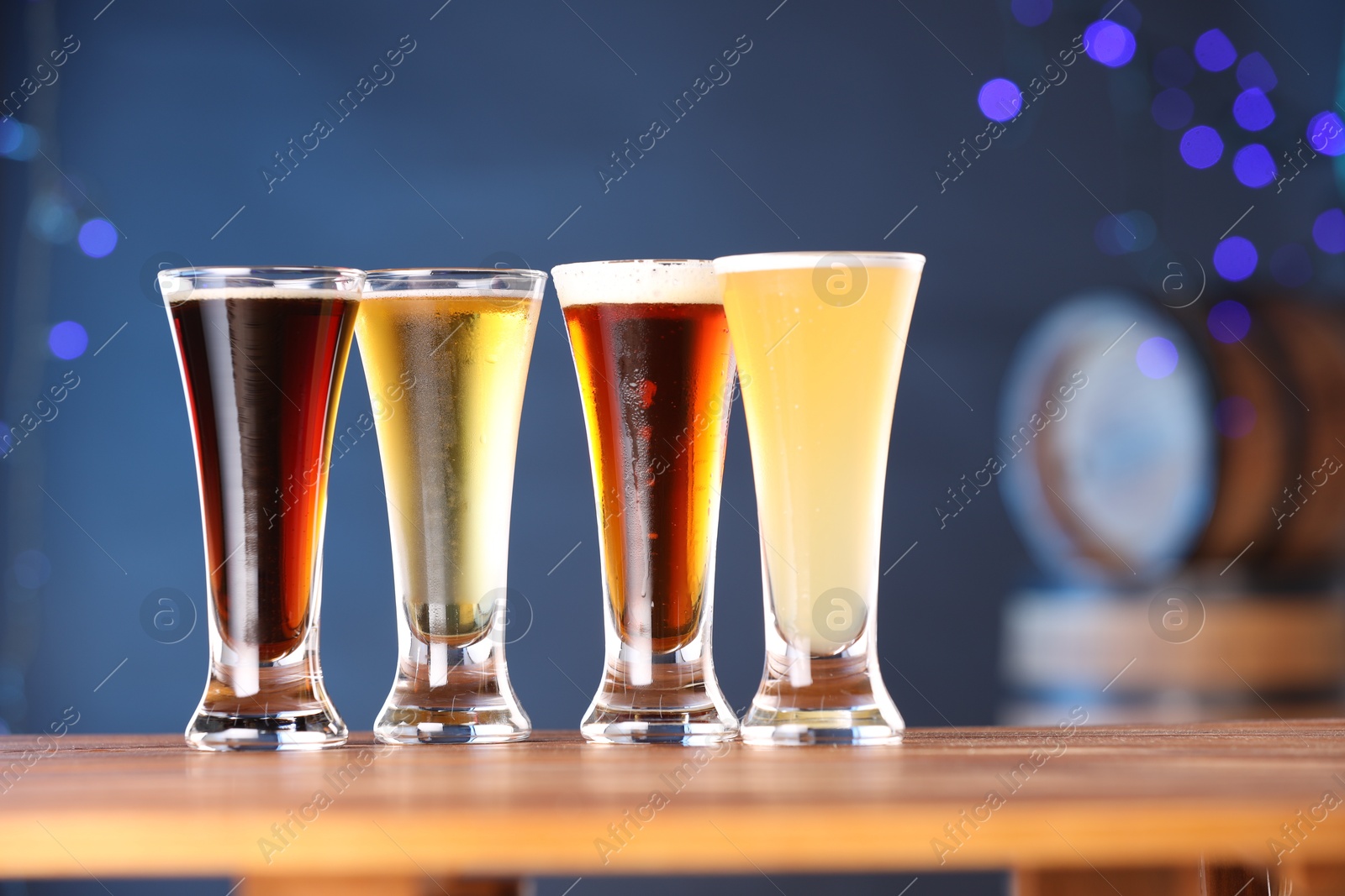 Photo of Glasses with different types of beer on wooden table against blue background, closeup